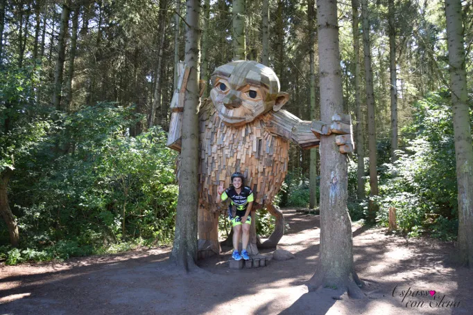 Ciclista posa davanti a un gigante di legno nascosto nel bosco