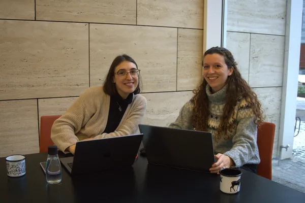Elena (a sinistra) e Giulia (a destra) sedute a un tavolo con laptop e tazze di caffè