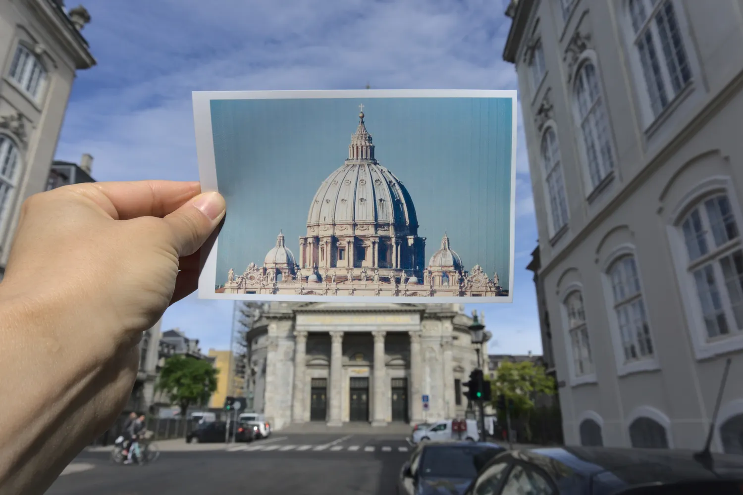 Cartolina della cupola di San Pietro tenuta davanti a un edificio cittadino