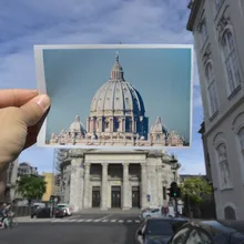 Cartolina della cupola di San Pietro tenuta davanti a un edificio cittadino