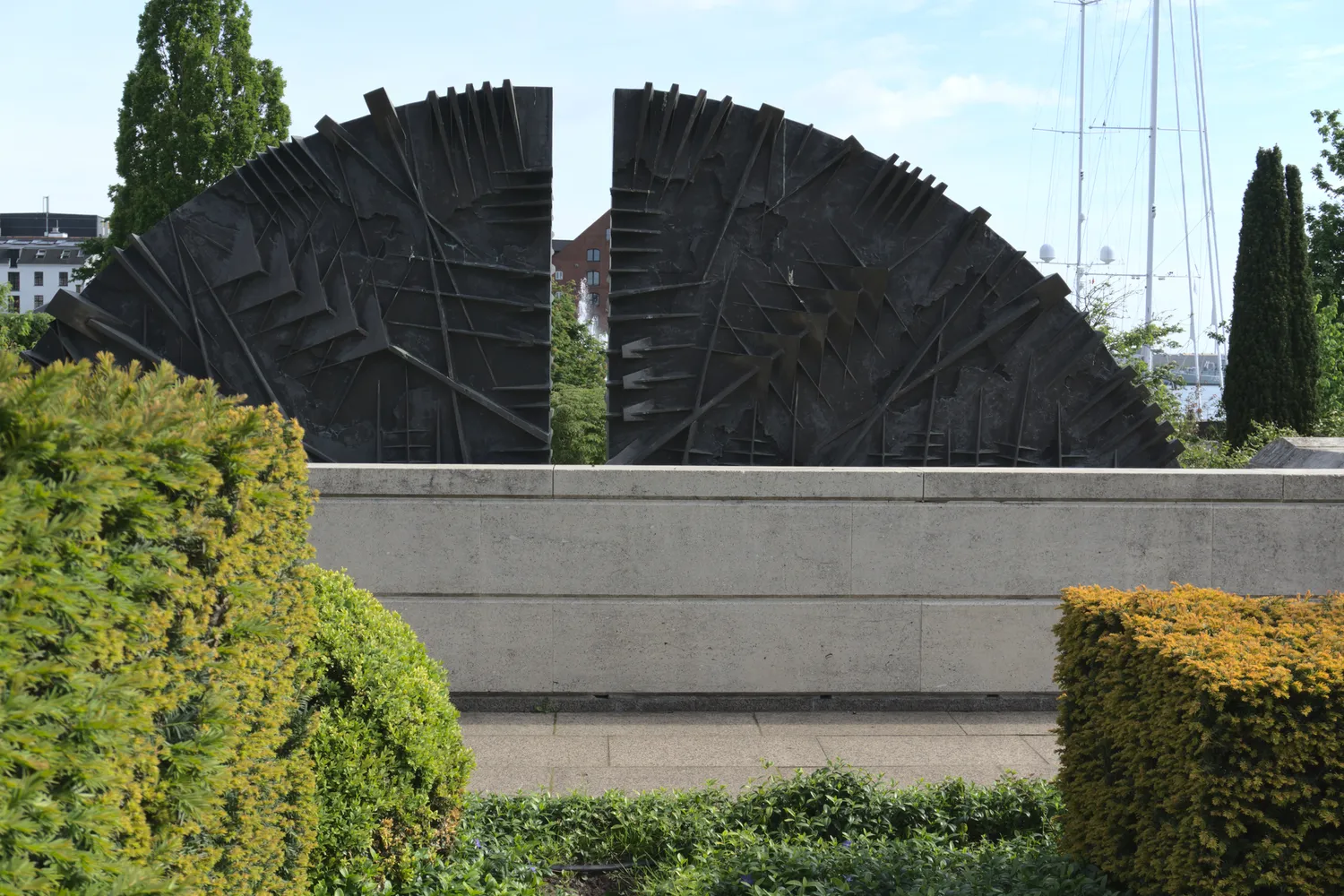Scultura astratta in bronzo a forma di ventaglio su muro di pietra