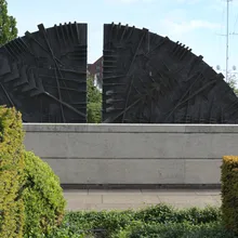 Scultura astratta in bronzo a forma di ventaglio su muro di pietra