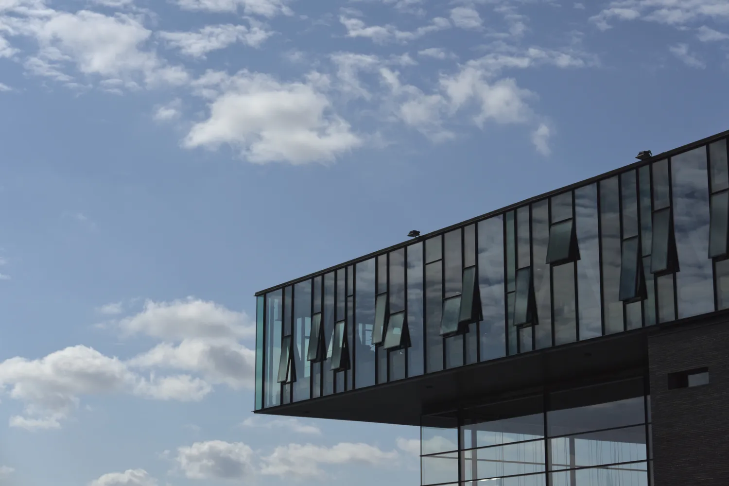 Edificio moderno con facciata vetrata sporgente contro un cielo azzurro nuvoloso