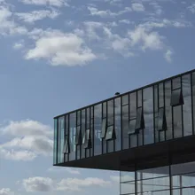 Edificio moderno con facciata vetrata sporgente contro un cielo azzurro nuvoloso