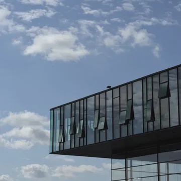Edificio moderno con facciata vetrata sporgente contro un cielo azzurro nuvoloso