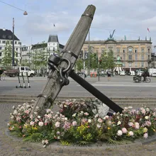 Grande ancora di legno e ferro circondata da fiori in una piazza