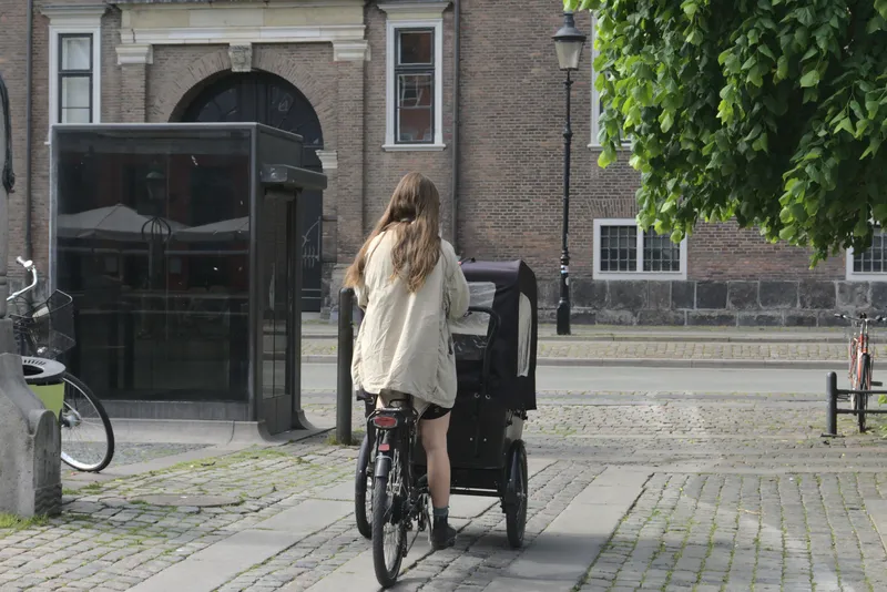 Donna pedala una cargo bike su strada acciottolata vicino a un edificio in mattoni
