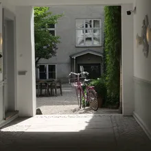 Cortile interno luminoso con bicicletta rosa visto da un androne