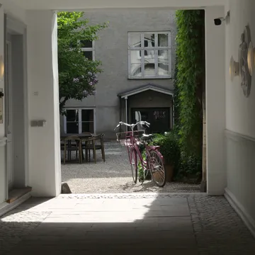 Cortile interno luminoso con bicicletta rosa visto da un androne