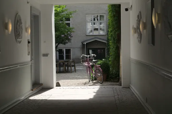 Cortile interno luminoso con bicicletta rosa visto da un androne