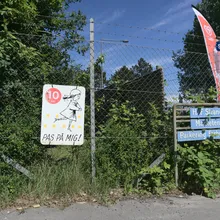 Recinzione con cartello giallo che invita a rallentare, vegetazione rigogliosa