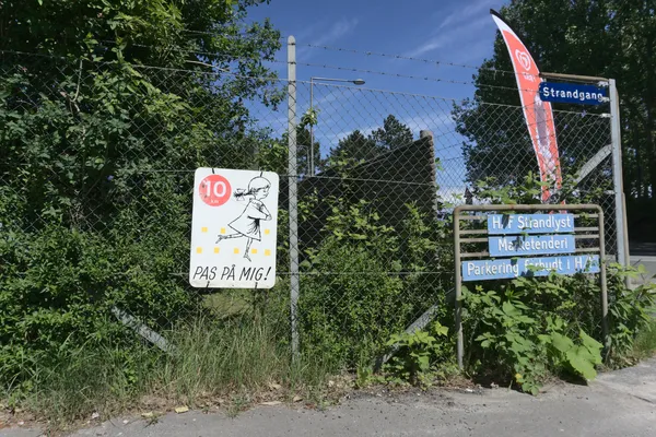 Recinzione con cartello giallo che invita a rallentare, vegetazione rigogliosa