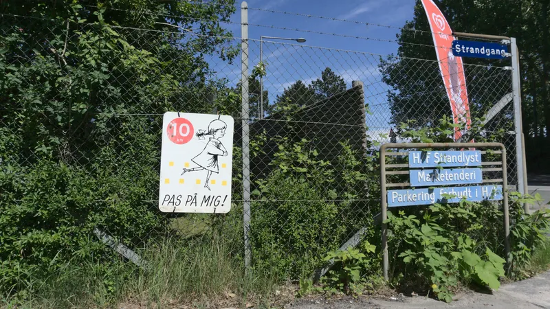 Recinzione con cartello giallo che invita a rallentare, vegetazione rigogliosa