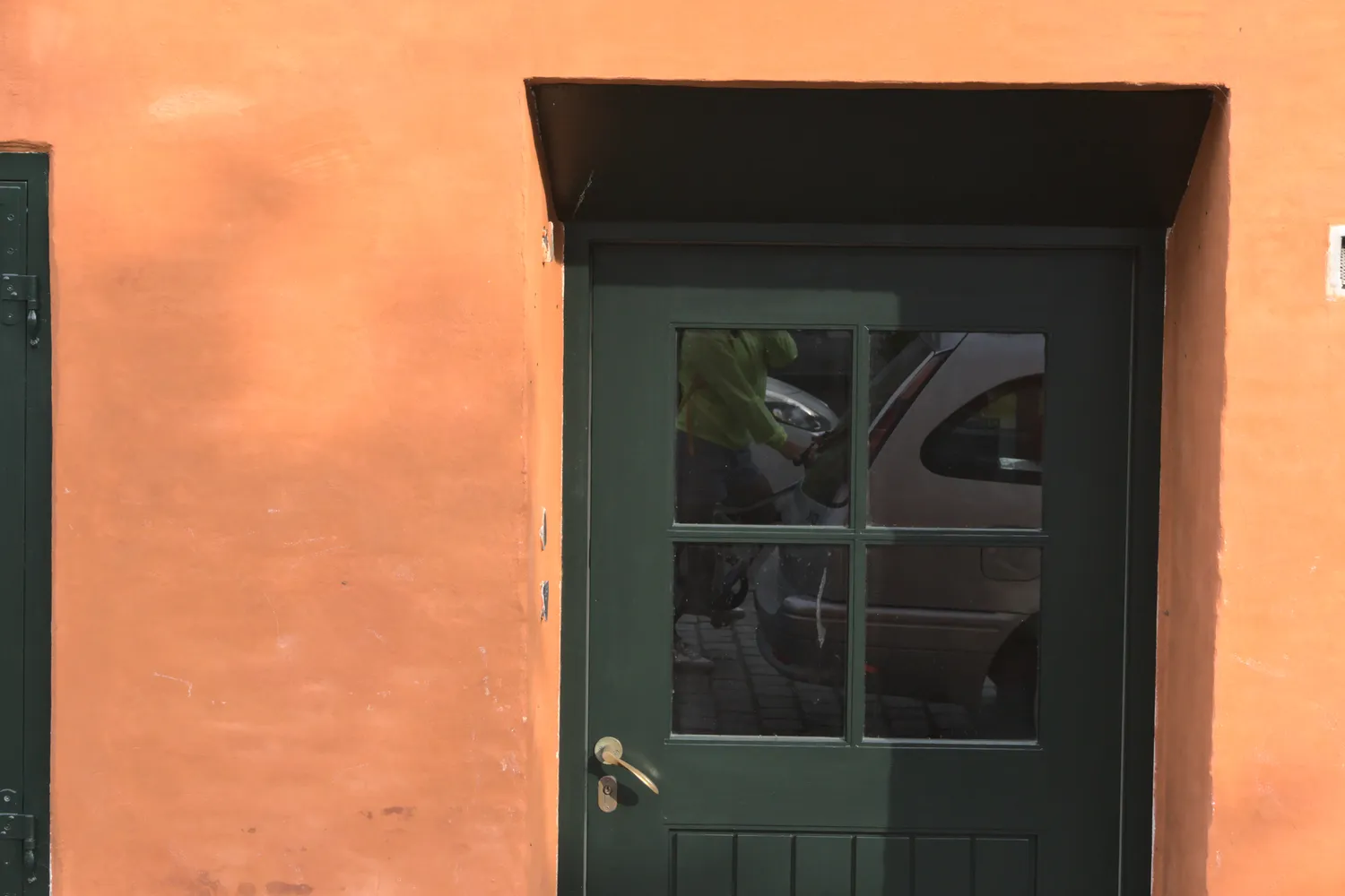 Porta verde in una parete arancione, con auto riflessa nel vetro