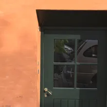 Porta verde in una parete arancione, con auto riflessa nel vetro