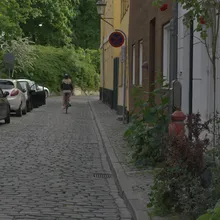 Ciclista in una stradina acciottolata di Christianshavn fiancheggiata da case colorate e auto parcheggiate
