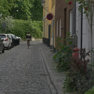 Ciclista in una stradina acciottolata di Christianshavn fiancheggiata da case colorate e auto parcheggiate