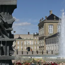 Dettaglio di scultura bronzea con palazzo e fontana zampillante sullo sfondo