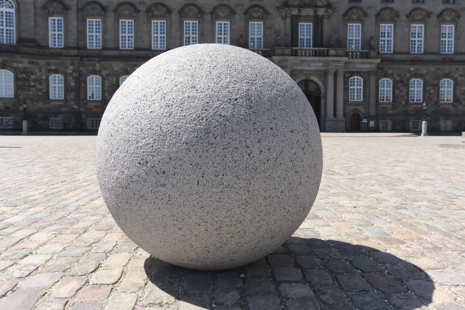 Grande sfera di granito su pavimentazione davanti a un palazzo storico