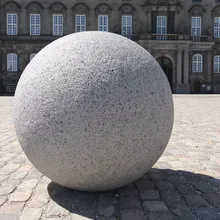 Grande sfera di granito su pavimentazione davanti a un palazzo storico