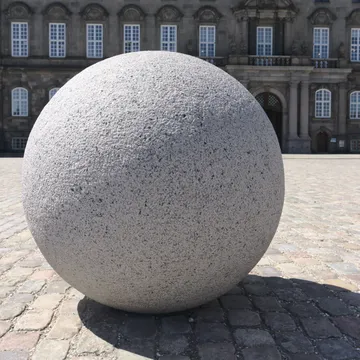 Grande sfera di granito su pavimentazione davanti a un palazzo storico