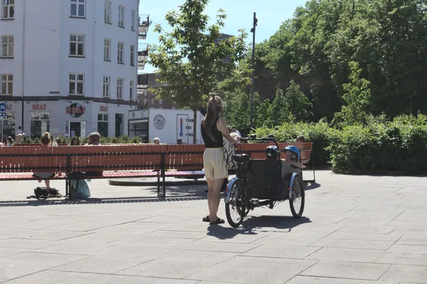 Donna ferma in piazza con una bici cargo e bambini a bordo