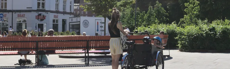 Donna ferma in piazza con una bici cargo e bambini a bordo
