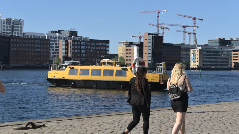 Due donne camminano sulla banchina mentre un battello giallo attraversa il porto