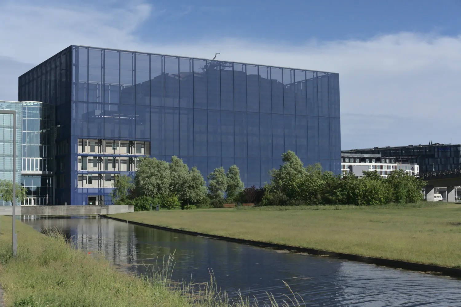 Edificio moderno con facciata in vetro scuro accanto a un canale erboso nel quartiere Ørestad