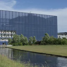 Edificio moderno con facciata in vetro scuro accanto a un canale erboso nel quartiere Ørestad
