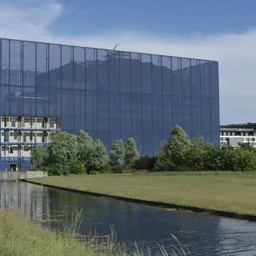 Edificio moderno con facciata in vetro scuro accanto a un canale erboso nel quartiere Ørestad