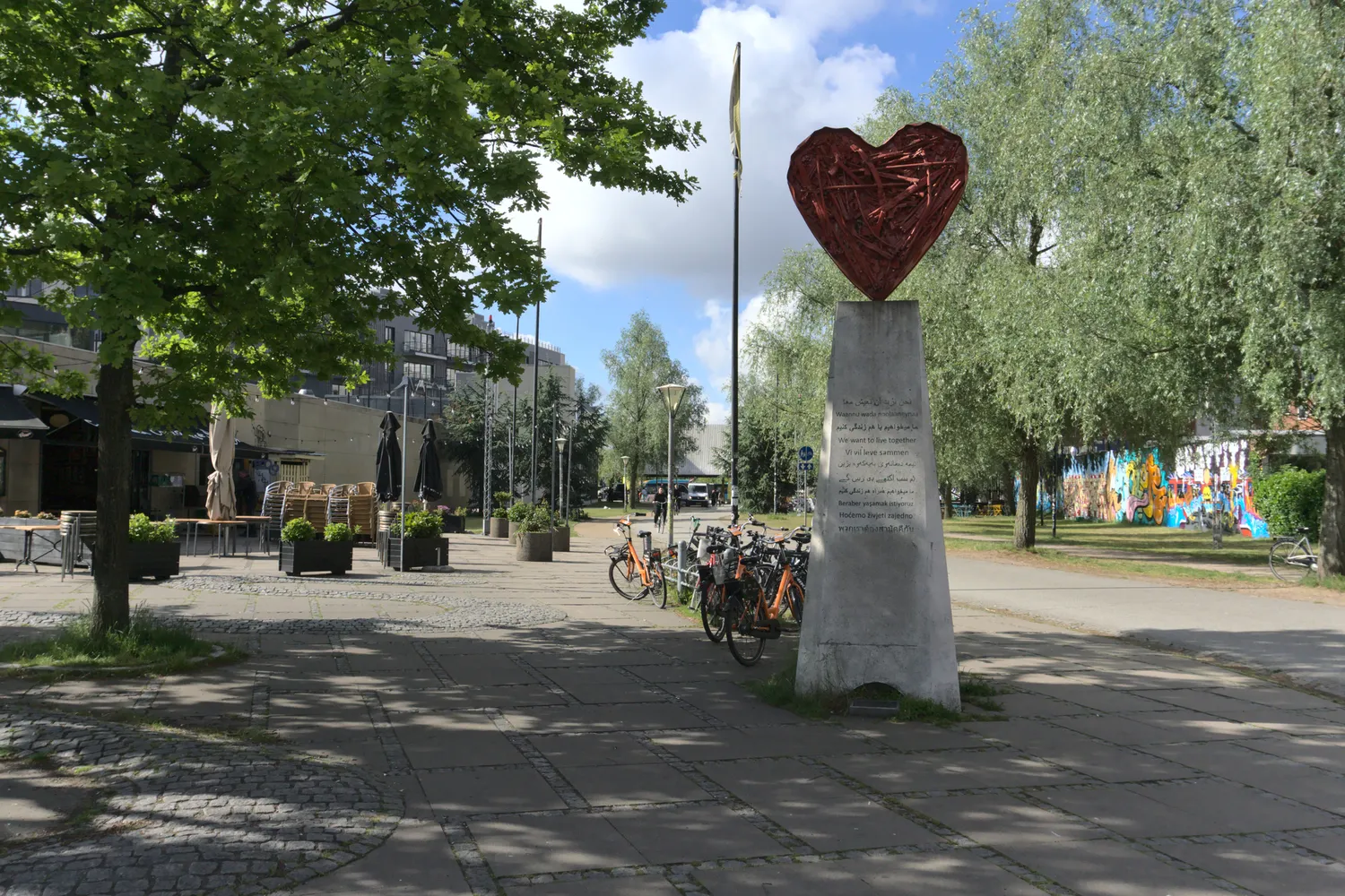 Scultura a forma di cuore rosso su colonna in una piazza alberata