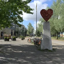 Scultura a forma di cuore rosso su colonna in una piazza alberata