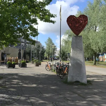 Scultura a forma di cuore rosso su colonna in una piazza alberata