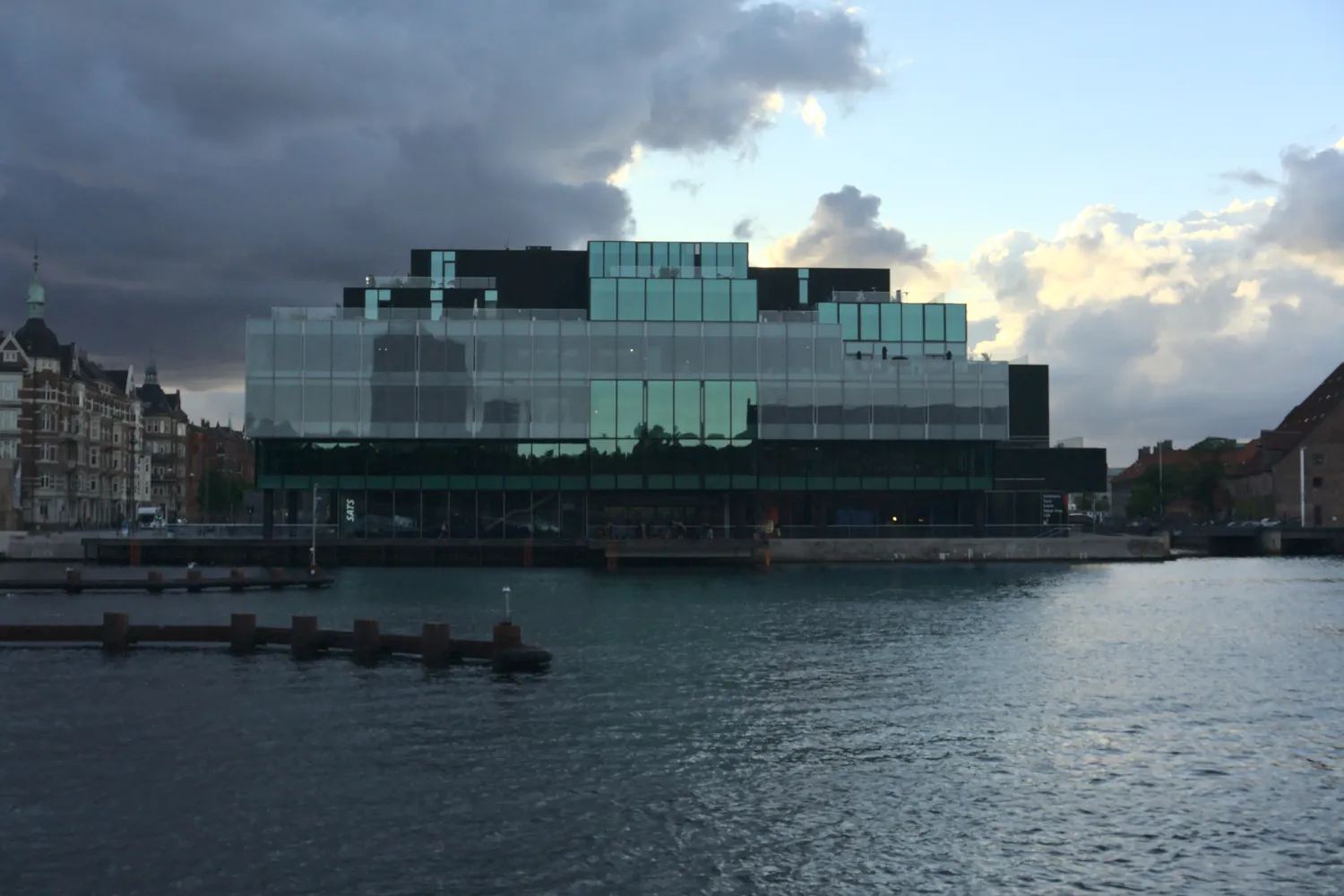 Edificio moderno in vetro sul lungomare sotto un cielo nuvoloso al tramonto