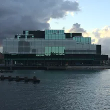 Edificio moderno in vetro sul lungomare sotto un cielo nuvoloso al tramonto