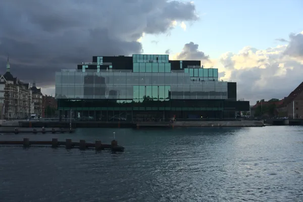 Edificio moderno in vetro sul lungomare sotto un cielo nuvoloso al tramonto