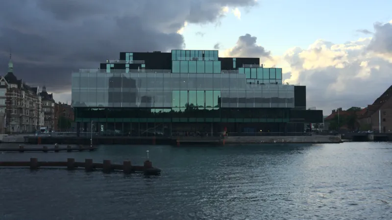 Edificio moderno in vetro sul lungomare sotto un cielo nuvoloso al tramonto
