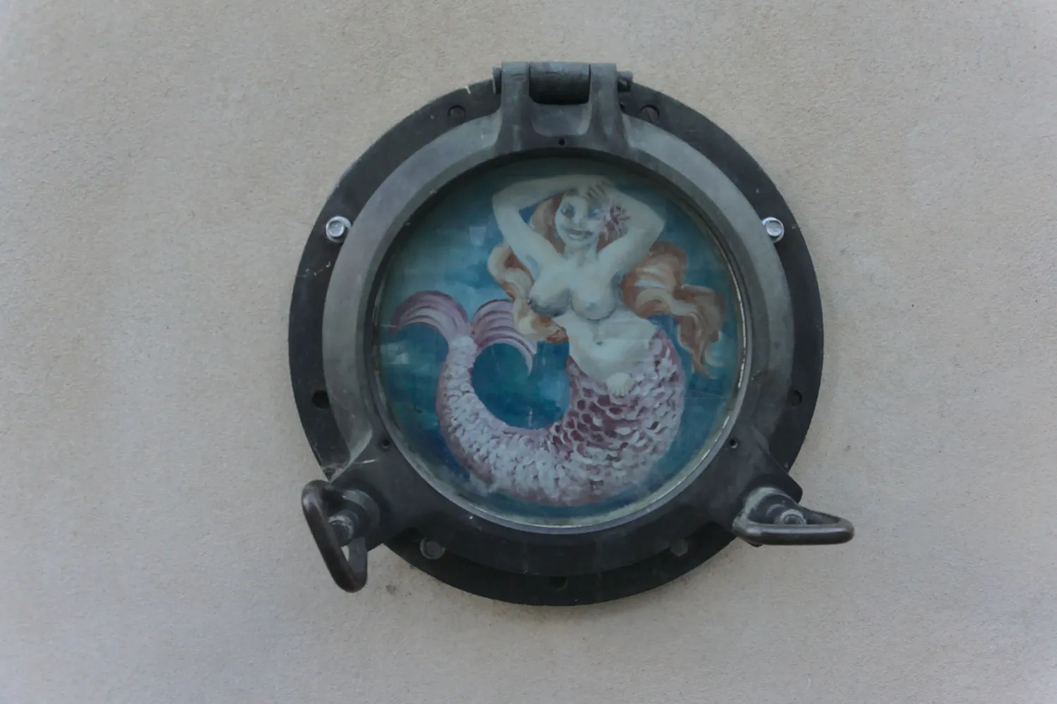 Oblò di nave su muro con dipinta una sirena dai capelli rossi