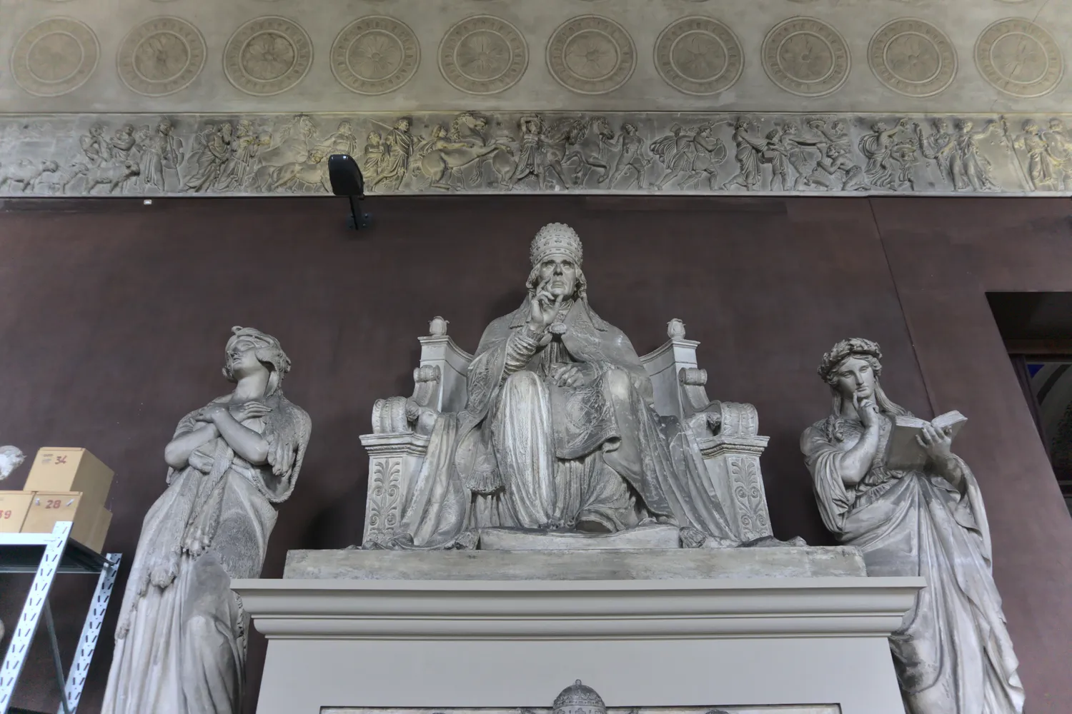 Scultura di un papa seduto in trono affiancato da figure femminili