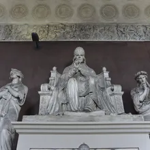 Scultura di un papa seduto in trono affiancato da figure femminili