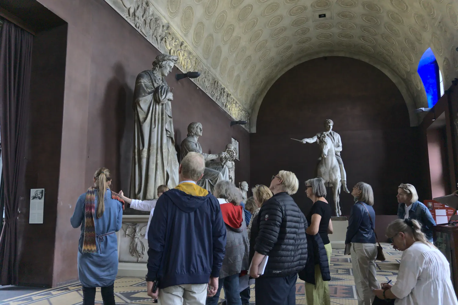 Gruppo guidato osserva grandi statue e un cavaliere in una sala museale