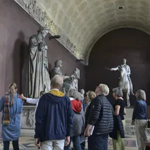 Gruppo guidato osserva grandi statue e un cavaliere in una sala museale