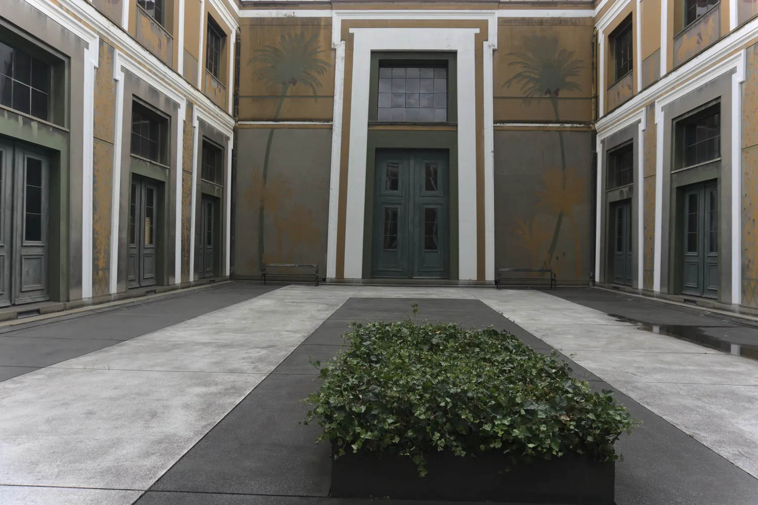 Cortile interno con murali di palme e una siepe verde squadrata