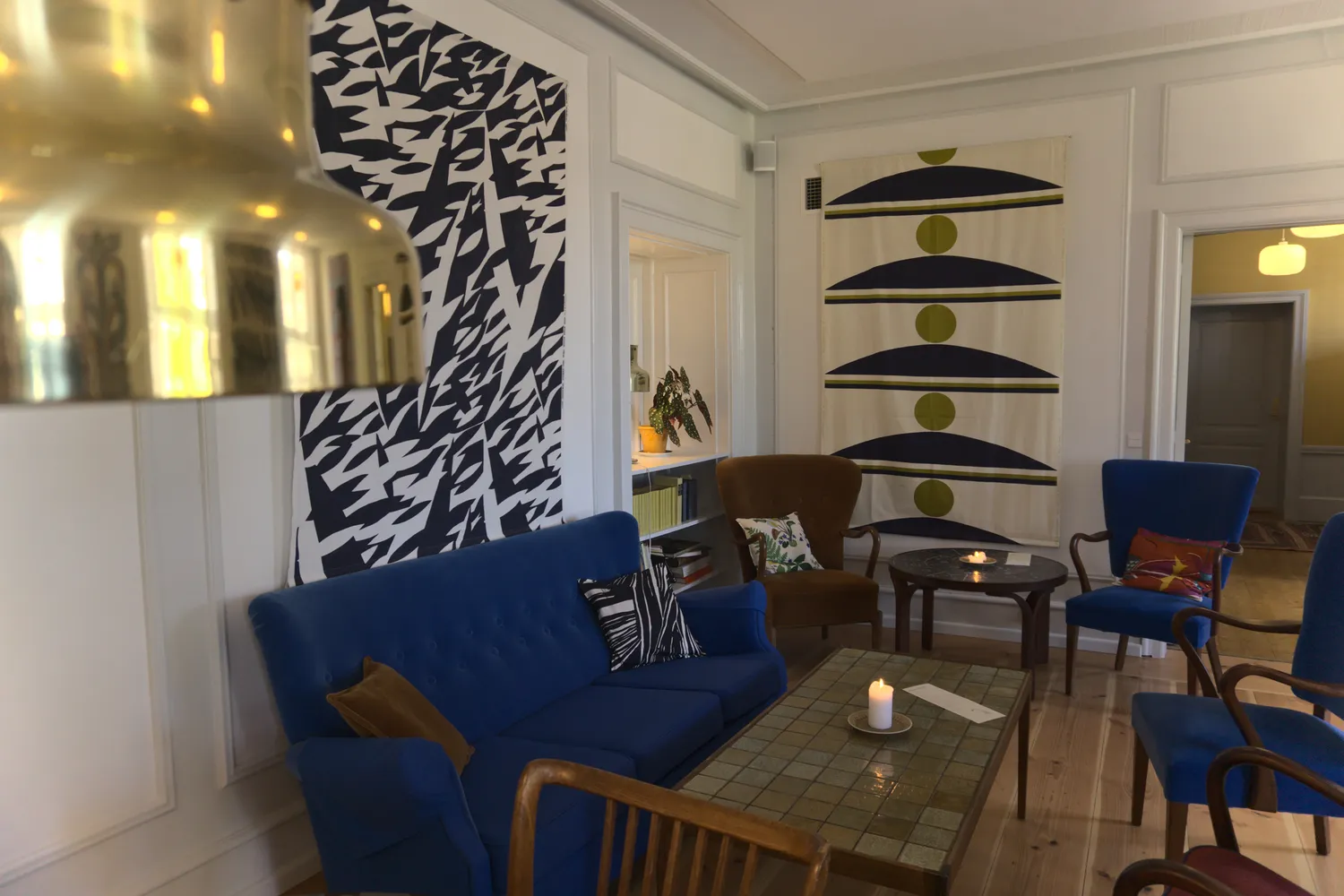 Salotto danese con divano blu, arazzi grafici e lampada in ottone