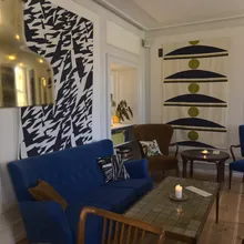 Salotto danese con divano blu, arazzi grafici e lampada in ottone