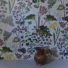 Brocca di ceramica marrone davanti a una parete con carta da parati floreale