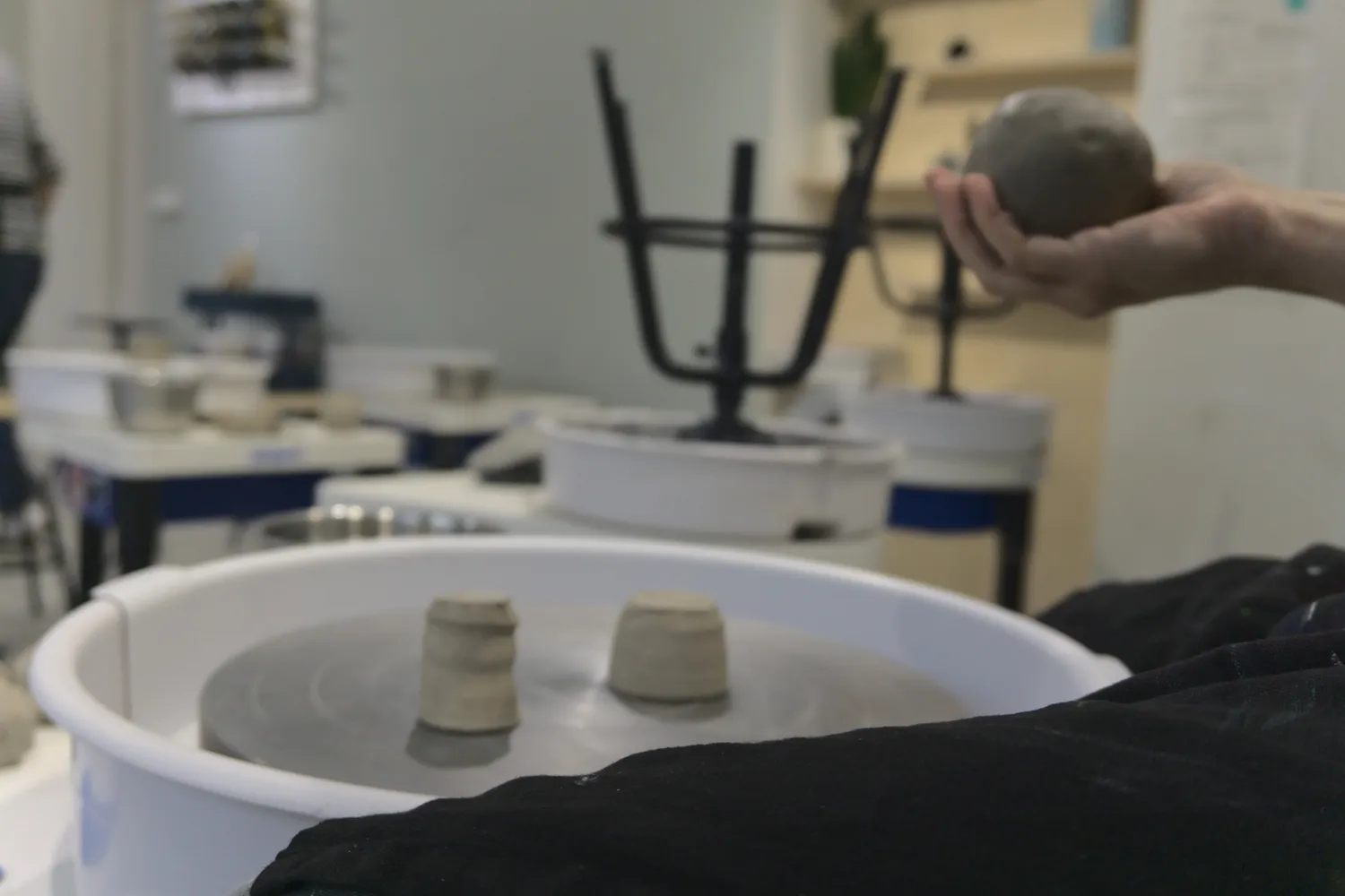 Tornio da ceramica con piccoli vasi e mano che impasta una palla di argilla