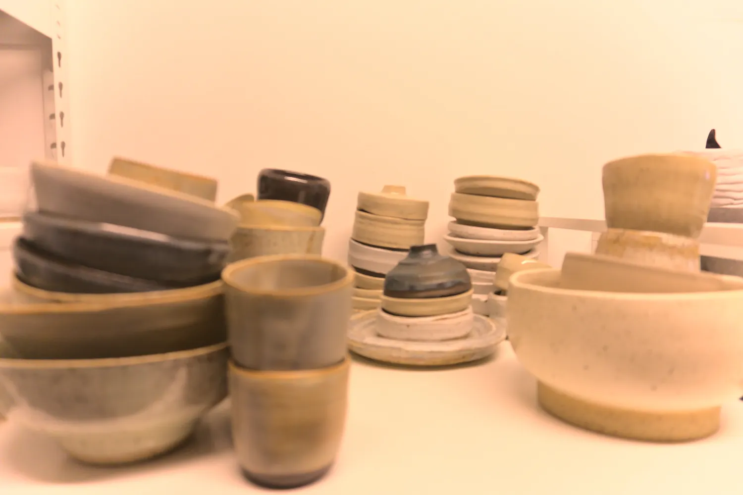 Ciotole e tazze di ceramica artigianale dai toni neutri su uno scaffale bianco