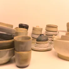 Ciotole e tazze di ceramica artigianale dai toni neutri su uno scaffale bianco